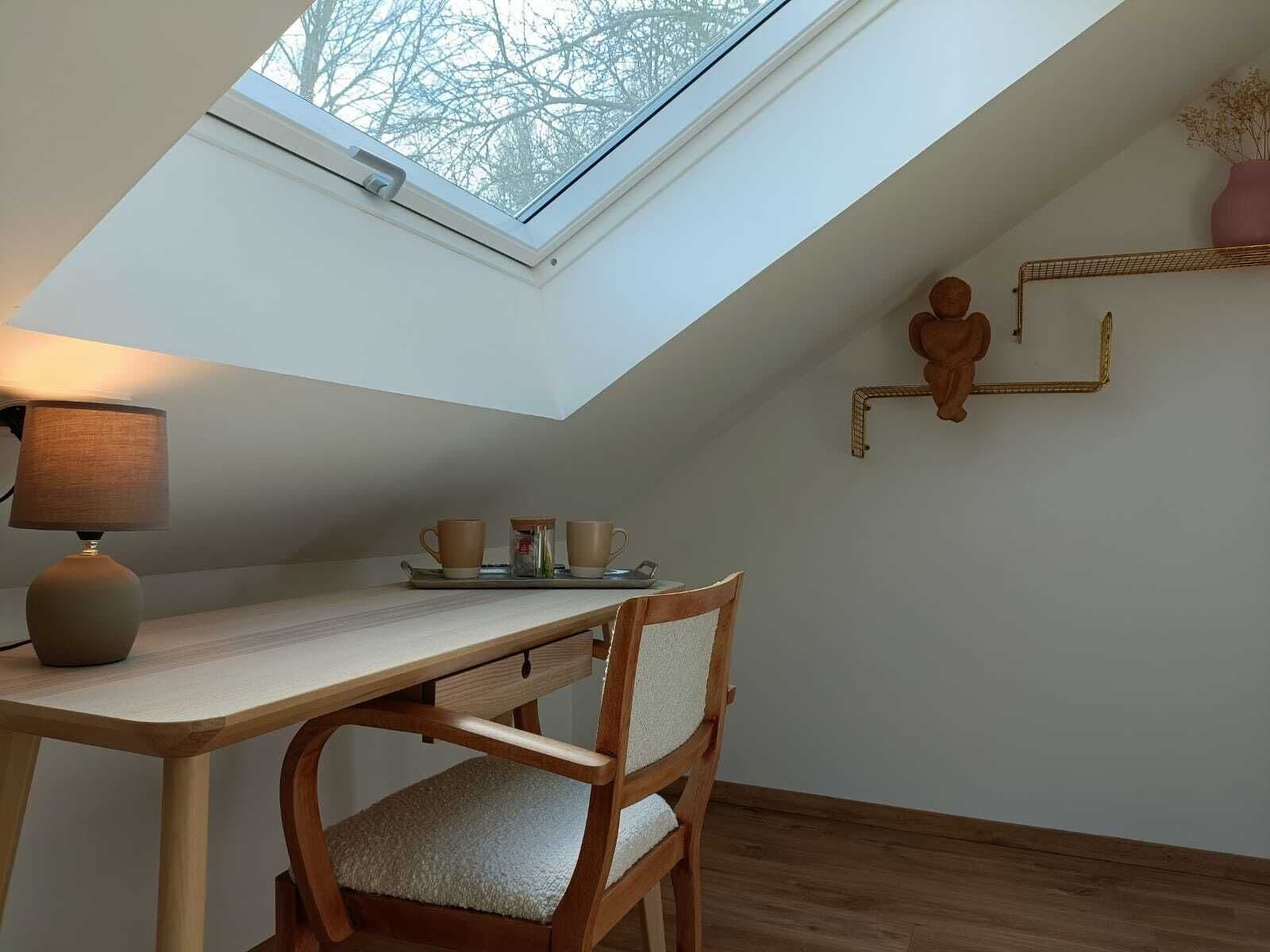 A cozy attic bedroom with a skylight, a wooden desk, a chair, and a small shelf with decorative items.