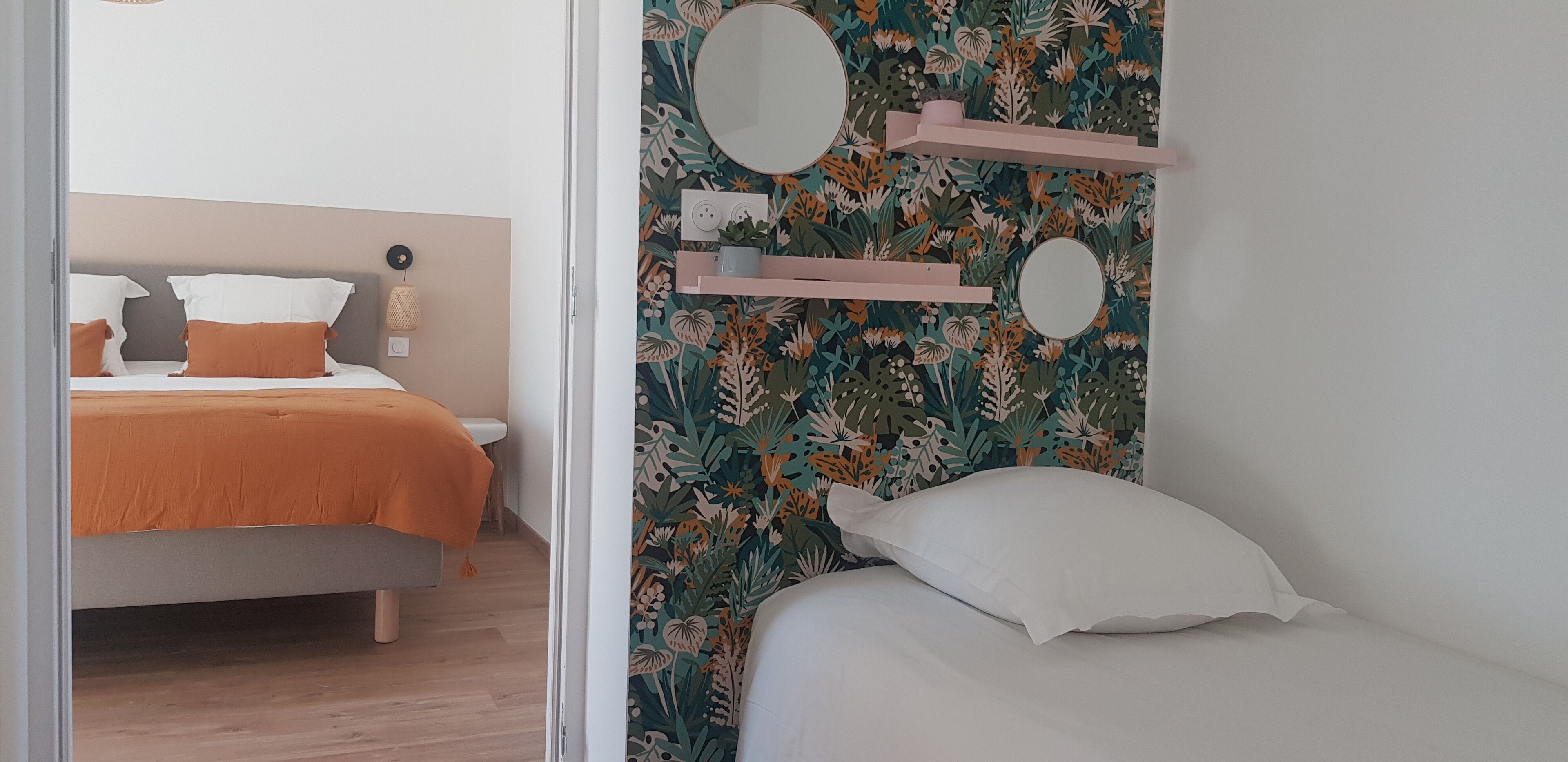 Une chambre à coucher avec un lit, une table de chevet, un miroir et un mur orné d’un motif floral.