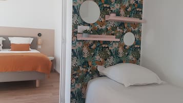 Une chambre à coucher avec un lit, une table de chevet, un miroir et un mur orné d’un motif floral.