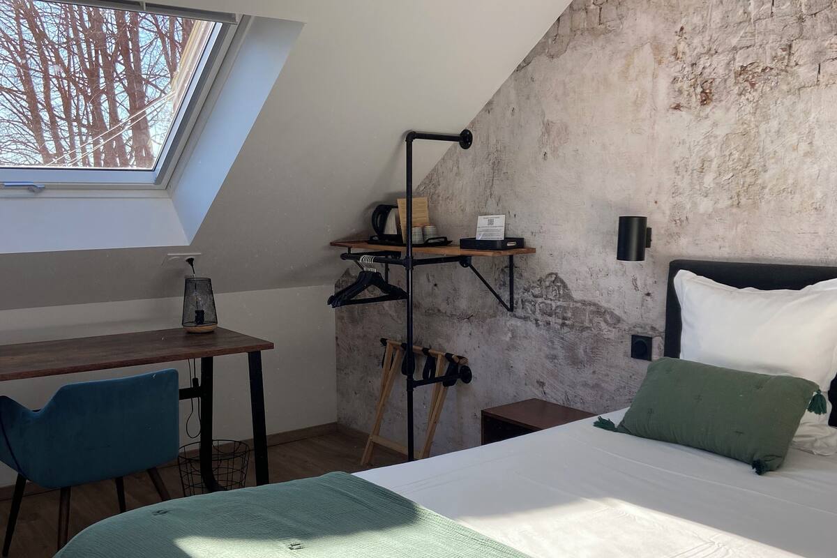 A bedroom with a skylight, a bed with a green blanket, a desk, and a wardrobe.
