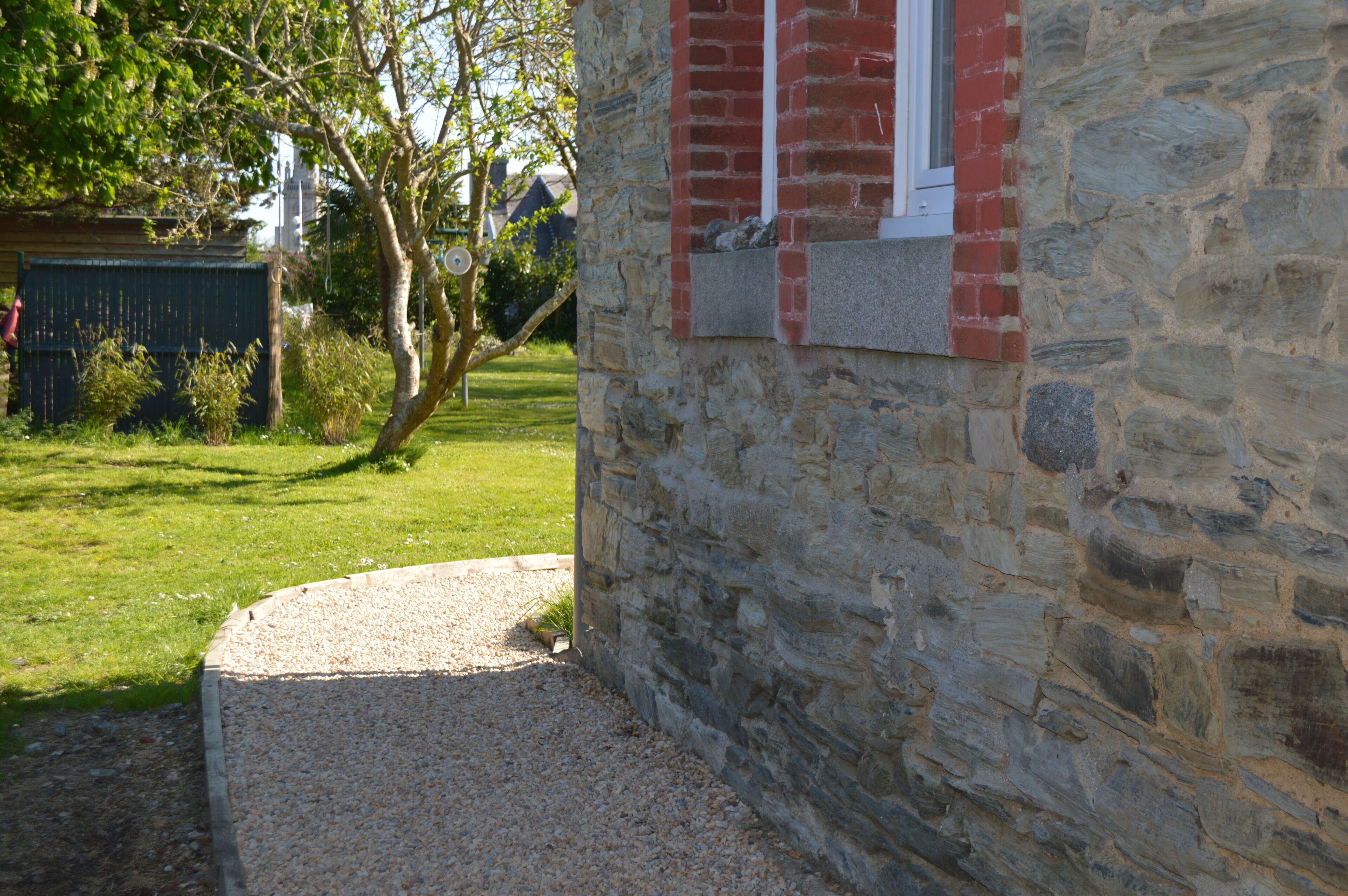 A stone building with a red window and a gravel path leading to it.