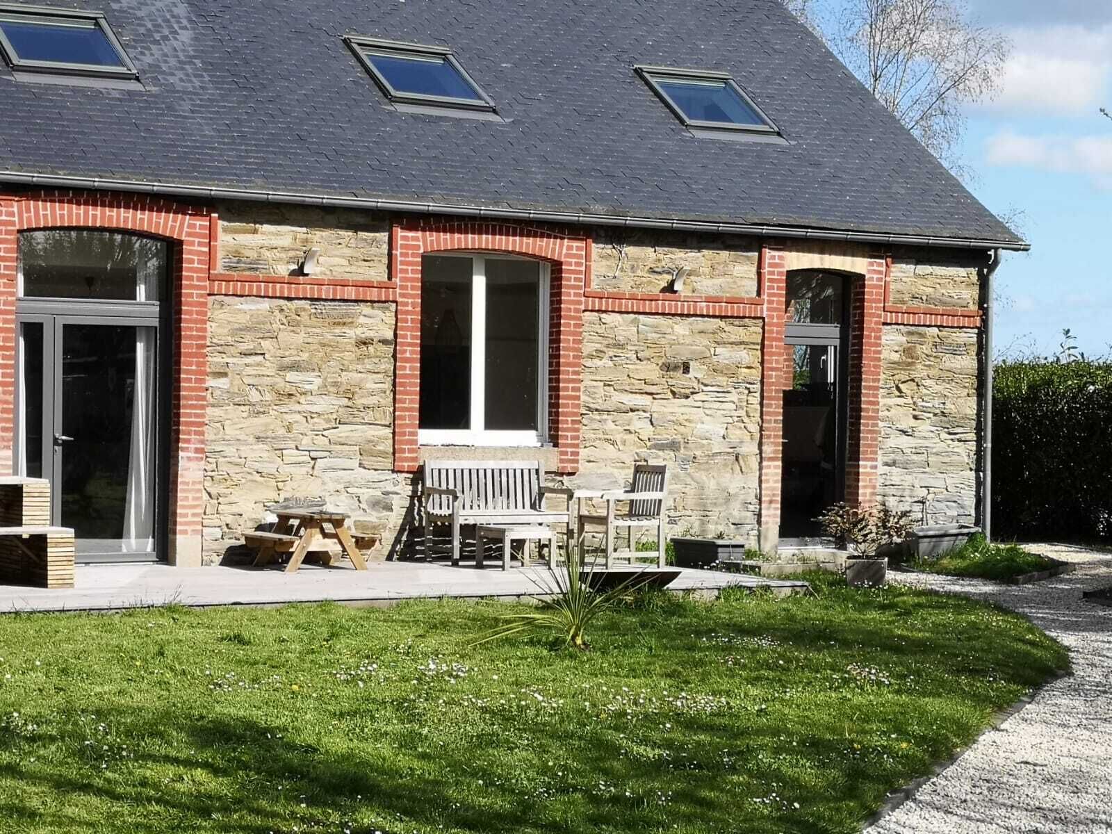 Een huis met twee verdiepingen, een gevel van natuursteen, een veranda met een bankje en een kleine tuin.