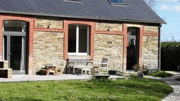 Een huis met twee verdiepingen, een gevel van natuursteen, een veranda met een bankje en een kleine tuin.