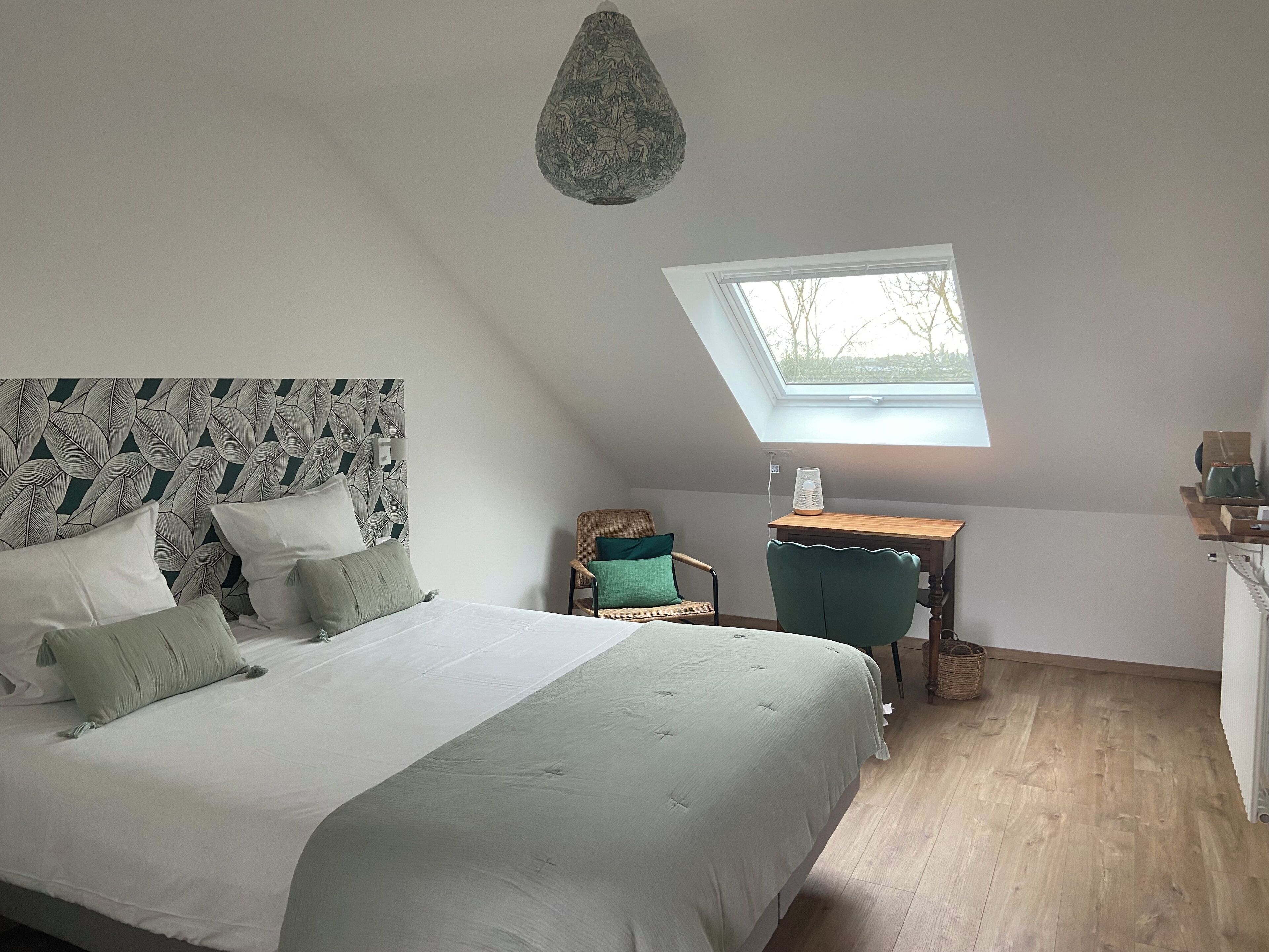 A bedroom with a bed, a desk, a chair, and a skylight.