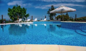 A swimming pool with clear blue water, surrounded by white lounge chairs and a large umbrella. -  Delta Nature Resort (Somova)