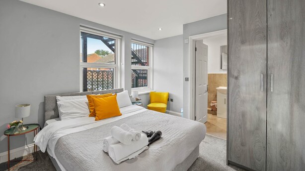 A modern bedroom with a large bed, a wardrobe, and a window with a view of a building.