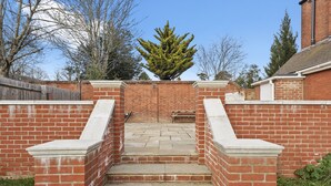 A brick staircase leading to a wooden bench in a garden area with a tree in the background.