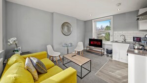 A modern living room with a yellow sofa, a small round table, and a TV displaying 'NETFLIX'.