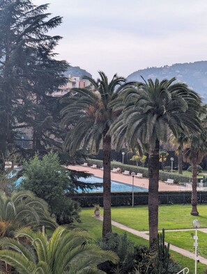 A pool area with palm trees and a view of buildings in the background. - Magnificent 2-room apartment with marina view near the sea (Mandelieu-la-Napoule)