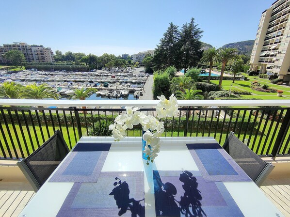 A balcony with a view of a marina, a pool, and surrounding greenery. - Magnificent 2-room apartment with marina view near the sea (Mandelieu-la-Napoule)