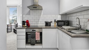 A modern kitchen with white cabinetry, a stainless steel range hood, a microwave, a toaster, and a dishwasher. - Luxurious Spacious Flat Maidstone with parking (Maidstone)