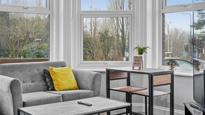 A modern living room with a grey sofa, a yellow pillow, a small table, and a TV. - Luxurious Spacious Flat Maidstone with parking (Maidstone)