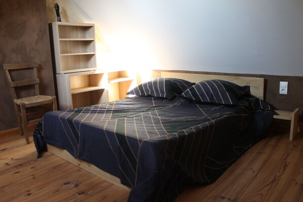 A bedroom with a bed, wooden floor, a chair, and a shelf unit. - The authentic and picturesque Gîte de la Tambourde. Overnight stays available upon request. (Lassouts)