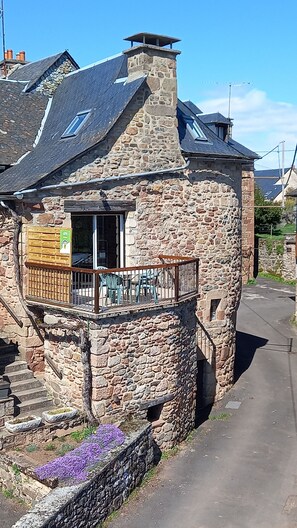A stone house with a balcony, a chimney, and a small garden with purple flowers. - The authentic and picturesque Gîte de la Tambourde. Overnight stays available upon request. (Lassouts)