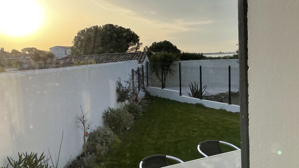 Une terrasse avec une table et des chaises, un sol carrelé en pierre, et une vue sur la mer et le paysage urbain au coucher du soleil.