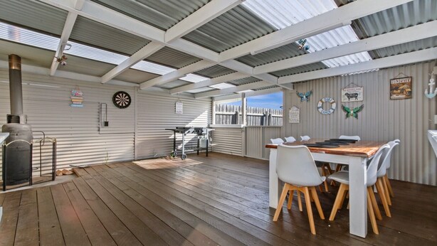 A covered outdoor area with a wooden deck, a table with chairs, and a dartboard.