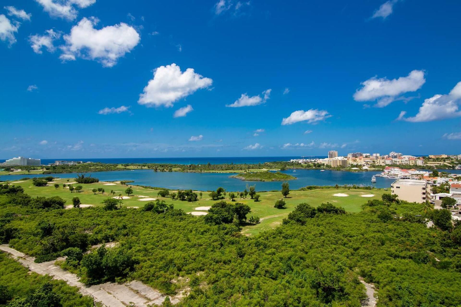 A coastal landscape with a golf course, a lake, and a cityscape in the background.