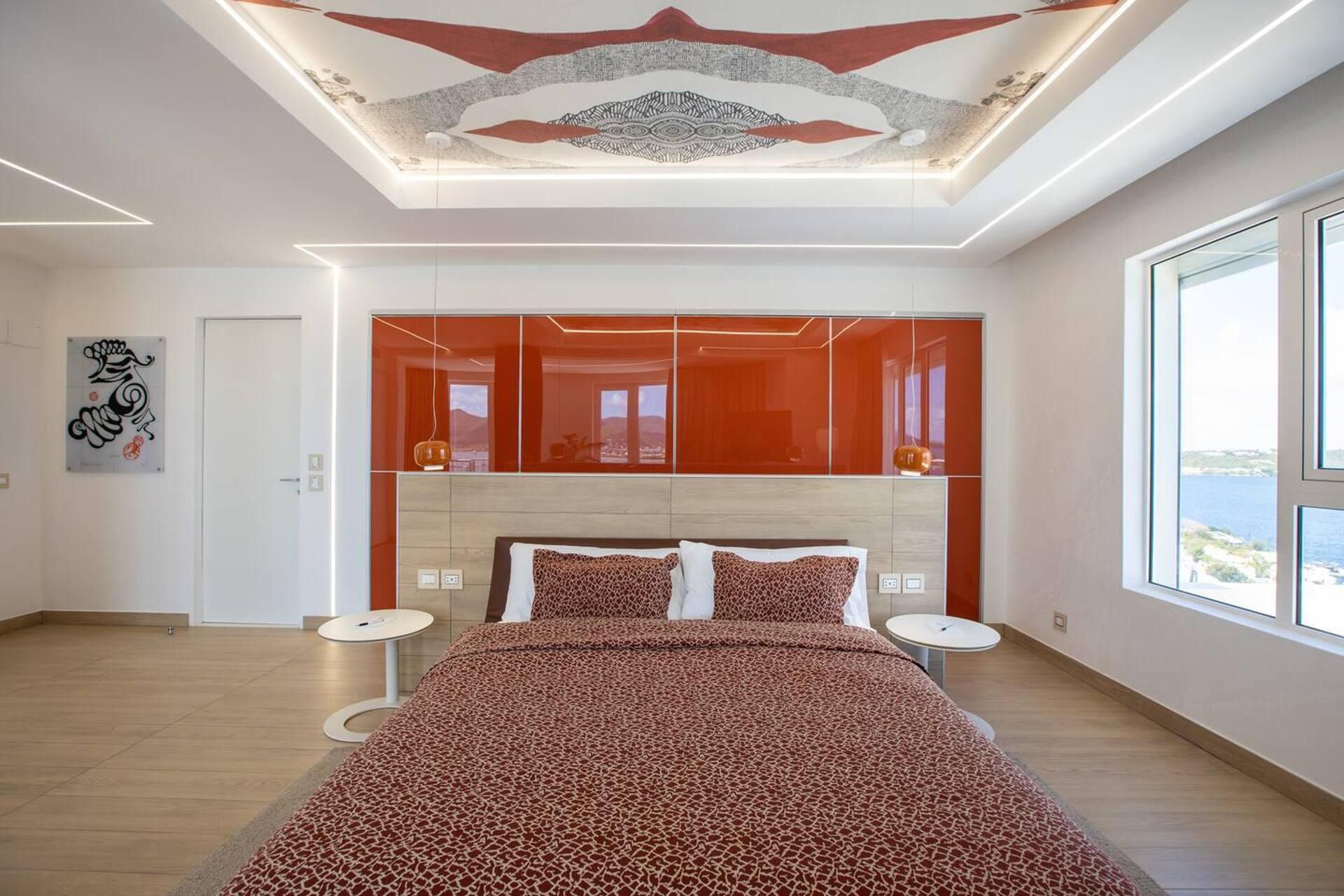 Ein modernes Schlafzimmer mit einem großen Bett, einer Decke mit geometrischem Muster und Meerblick durch ein großes Fenster.