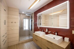 A modern bathroom with a large mirror, two sinks, and a walk-in shower.