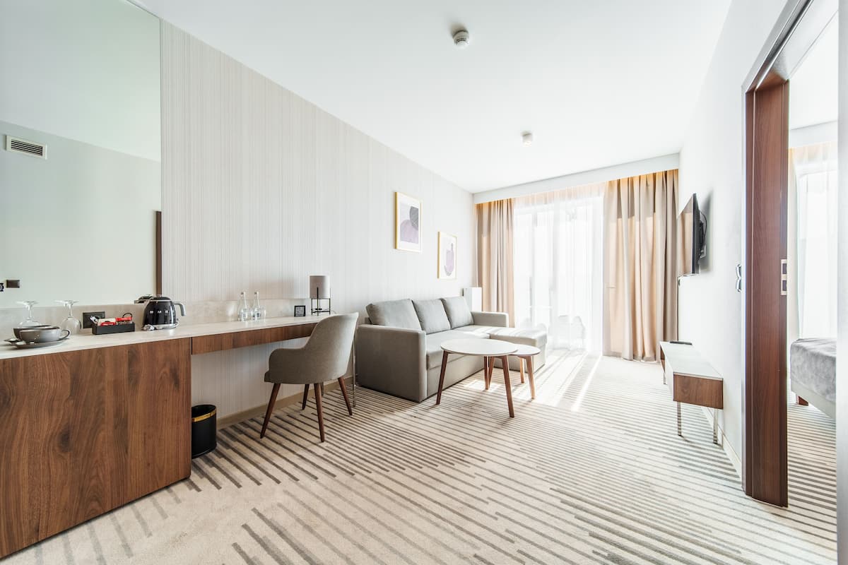 Ein modernes Hotelzimmer mit Küchenbereich, einer Couch, einem Esstisch und einem an der Wand befestigten Fernseher.