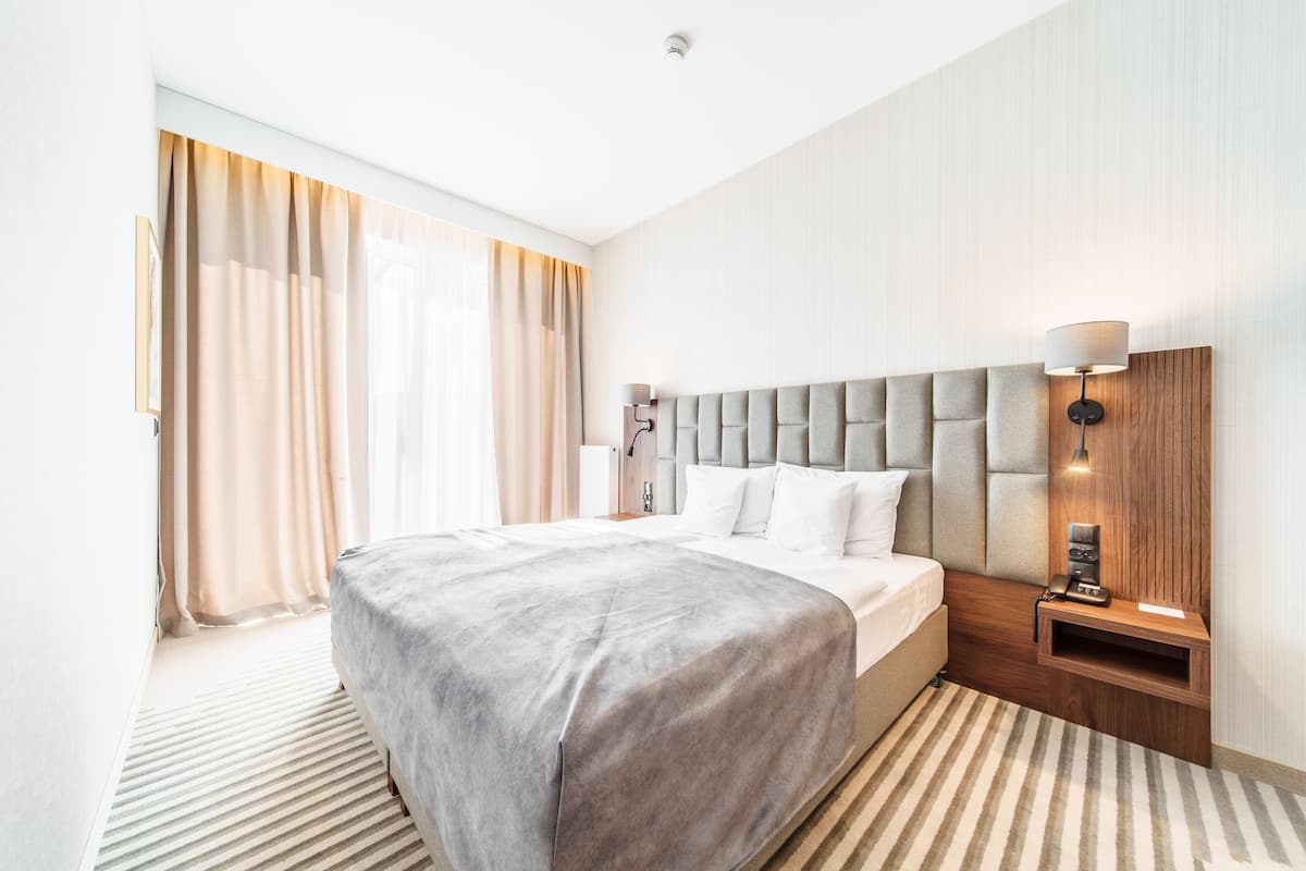 Ein modernes Hotelzimmer mit einem großen Bett, einem Nachttisch mit Lampe und einem Kopfteil mit integrierter Beleuchtung.