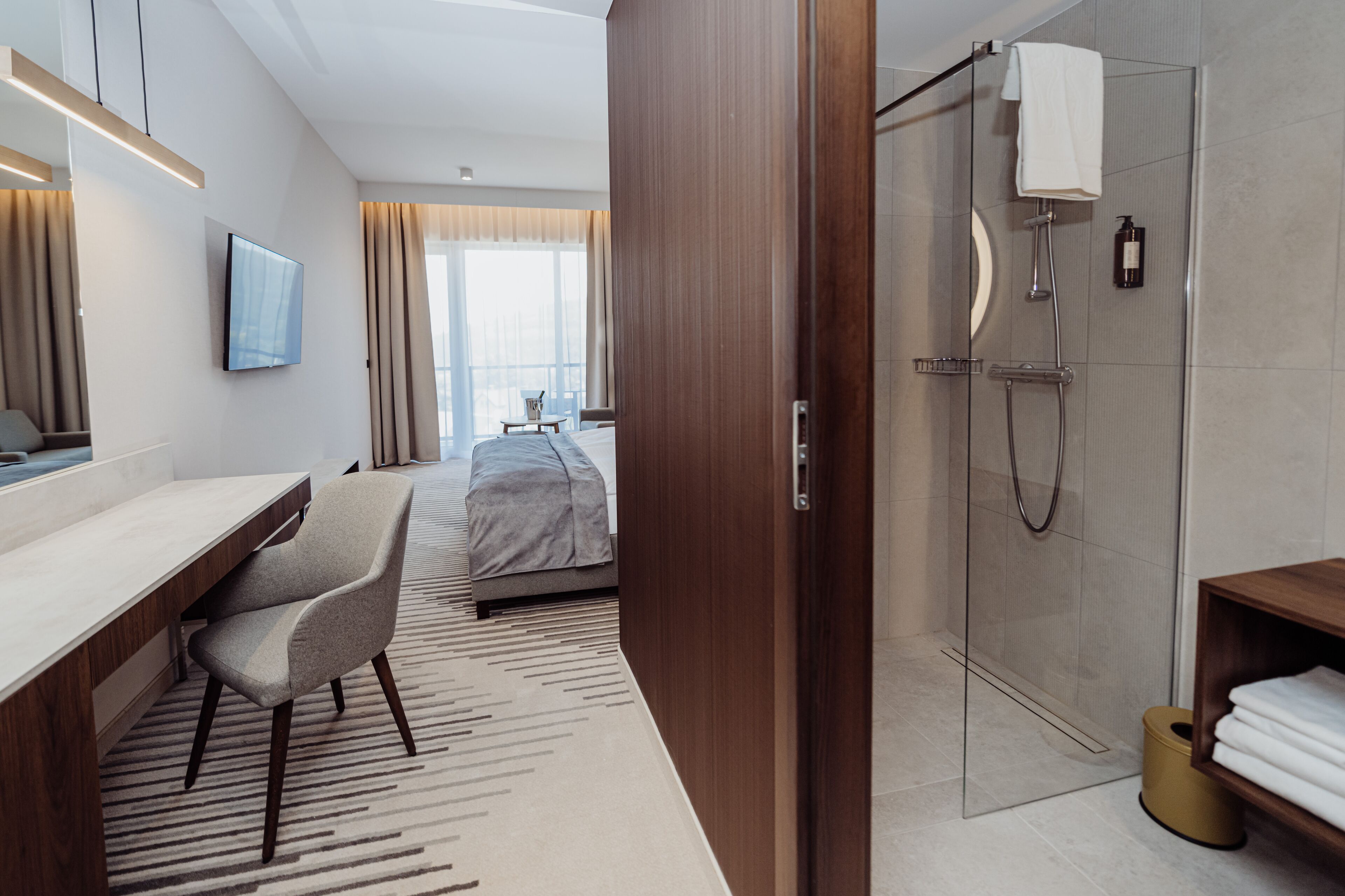Een moderne hotelkamer met een bed, bureau, stoel, televisie, douche en uitzicht op de stad.