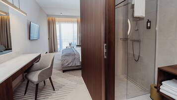 Een moderne hotelkamer met een bed, bureau, stoel, televisie, douche en uitzicht op de stad.