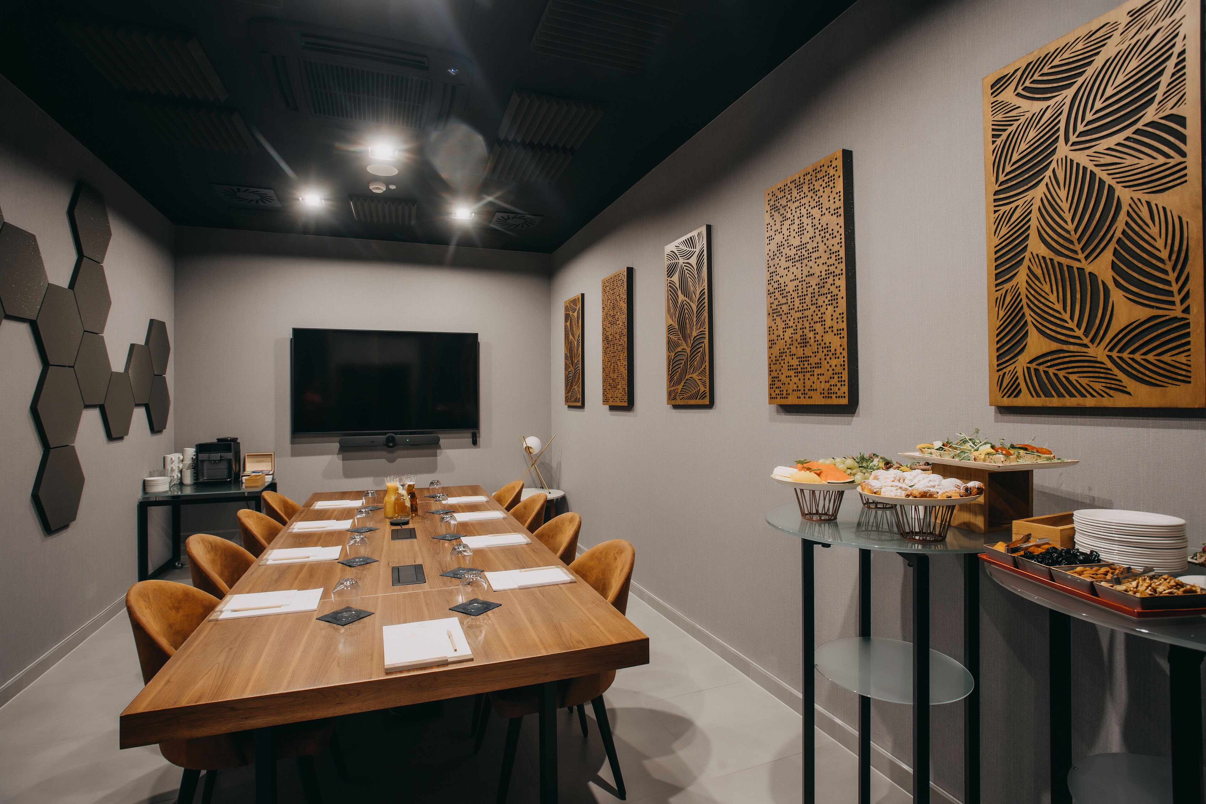 A conference room with a long table, chairs, a flat-screen TV, decorative panels, and a buffet table with food.