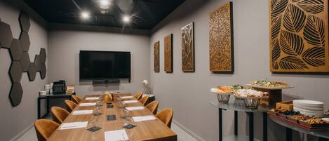 A conference room with a long table, chairs, a flat-screen TV, decorative panels, and a buffet table with food.