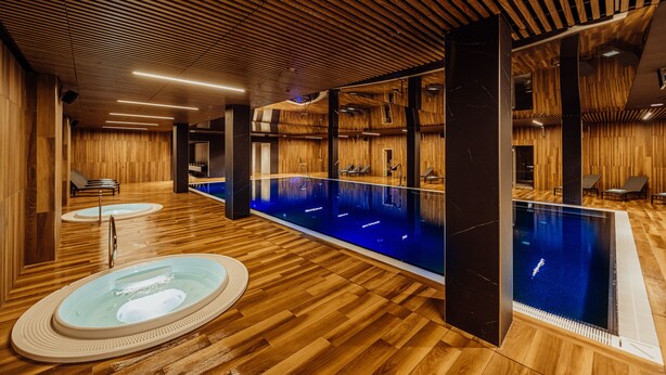 A modern indoor swimming pool with wooden flooring and walls, two hot tubs, and lounge chairs. - Elements Hotel Spa (Swieradow-Zdroj)