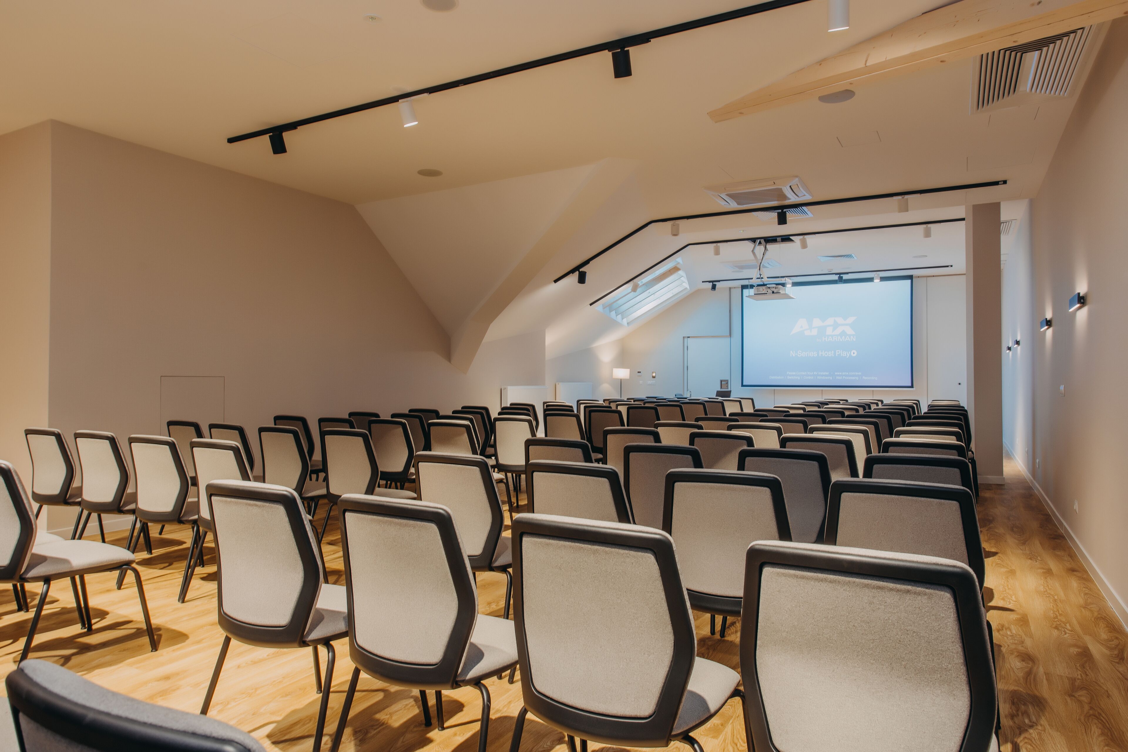 A conference room with rows of chairs, a projector screen, and a wooden floor.