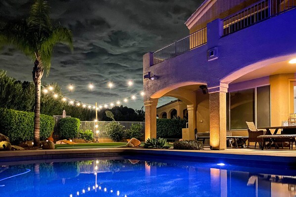 A pool with a clear reflection, a two-story building with balconies, and string lights in the background. - Spa, Putting Green! Family Haven in Fountain Hills (Fountain Hills)
