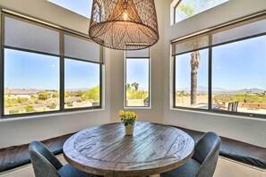 A round wooden table with a woven light fixture above, surrounded by cushioned seating, large windows with a view of a landscape, and a potted plant on the table. - Spa, Putting Green! Family Haven in Fountain Hills (Fountain Hills)