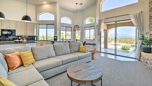 A spacious living area with a large sofa, a round coffee table, and a view of a pool and mountains through large windows. - Spa, Putting Green! Family Haven in Fountain Hills (Fountain Hills)
