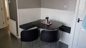 A small dining area with a round table, two black chairs, a clock on the wall, and a radiator.