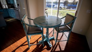 A dining area with a round table and four chairs, a small vase with a flower, and a view of a residential area through a glass door. - Lake Murray Lake Views Galore (Prosperity)