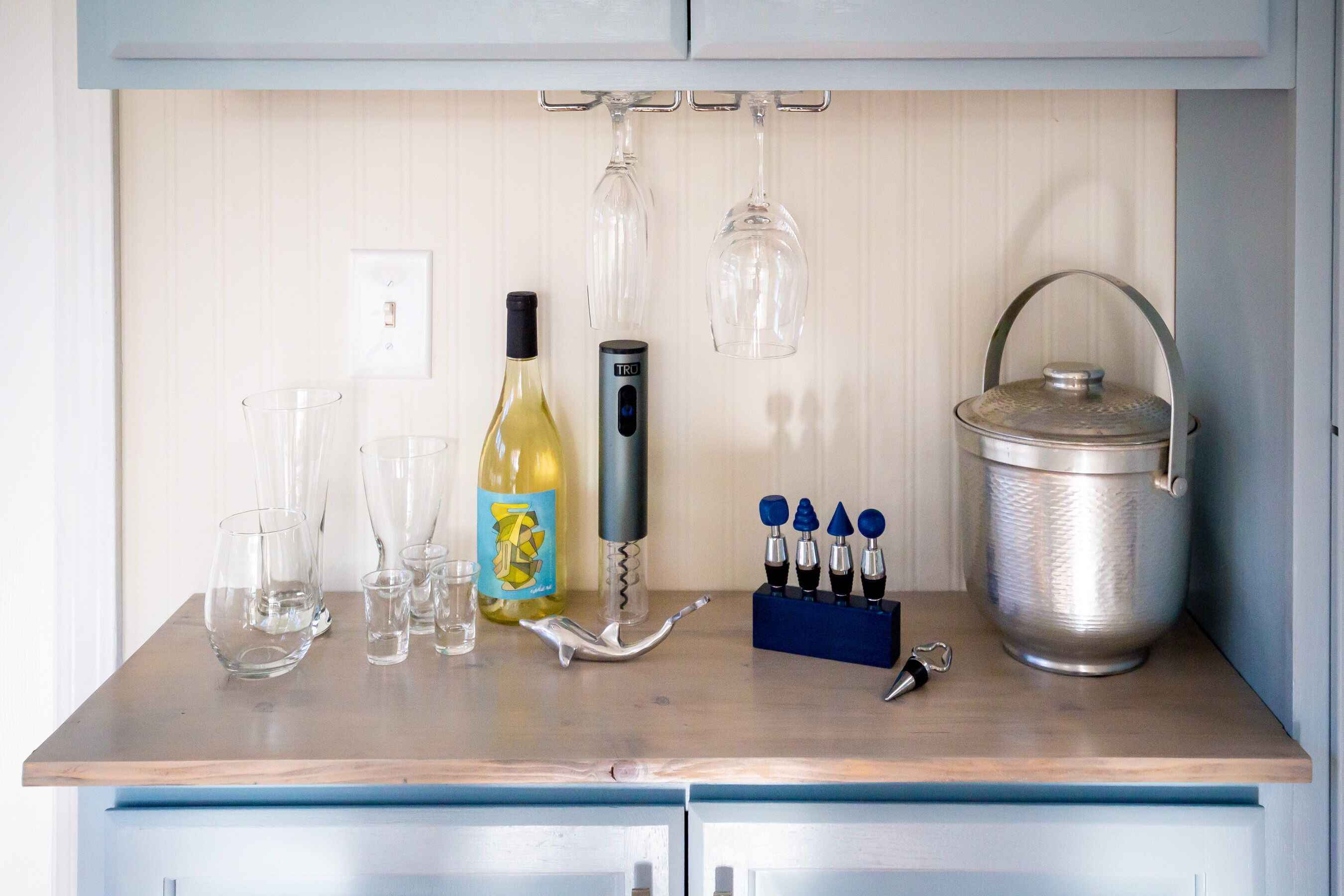 A kitchen counter with wine glasses, a wine bottle, a wine opener, and a set of corkscrews.