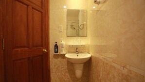 Un baño con puerta de madera, lavamanos, espejo y artículos de aseo en la encimera.