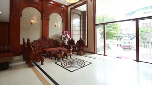 Un vestíbulo con una gran araña, un mostrador de recepción de madera y un área de descanso con muebles ornamentados.