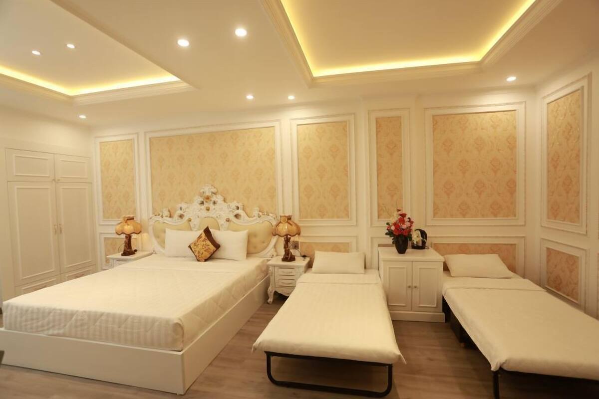 Ein Hotelzimmer mit einem großen Bett, einem kleineren Bett, zwei Einzelbetten, einem Nachttisch mit einer Lampe und einem Beistelltisch mit Blumen.