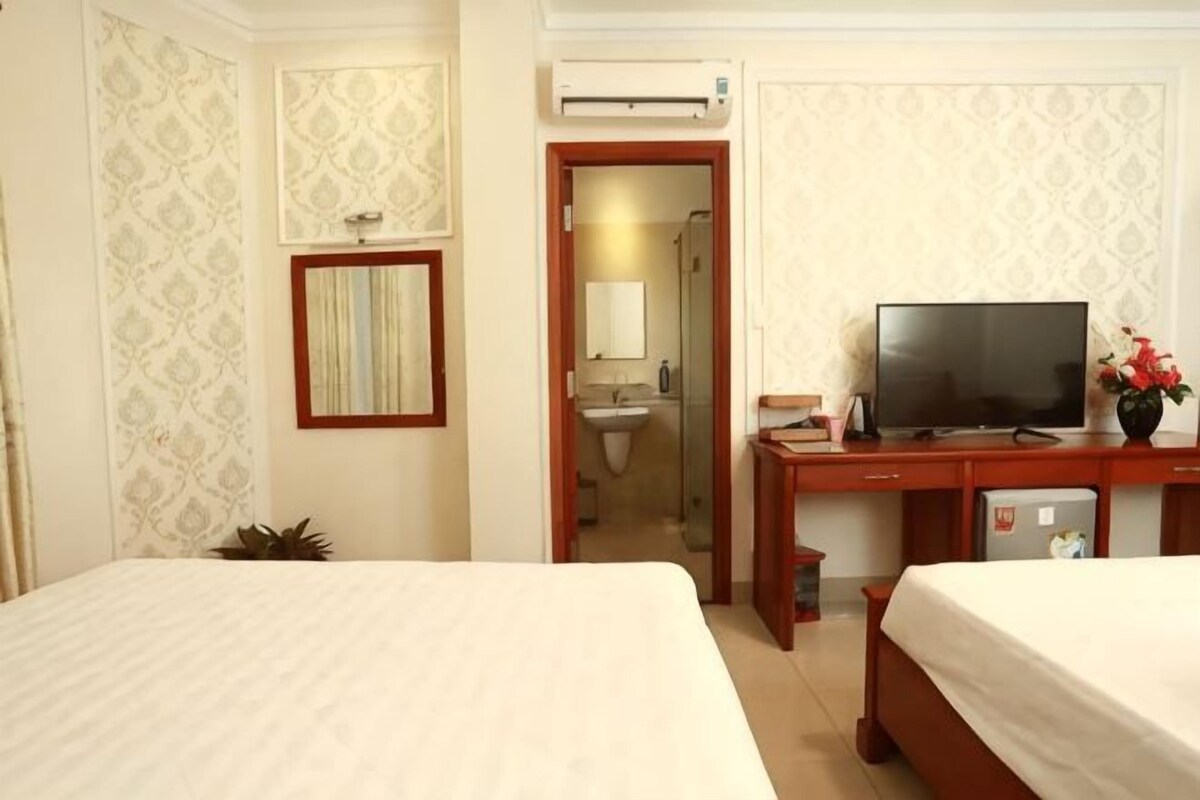 Ein Hotelzimmer mit zwei Betten, einem Fernseher, einem Schreibtisch mit Computer, einem Spiegel und einer Klimaanlage.