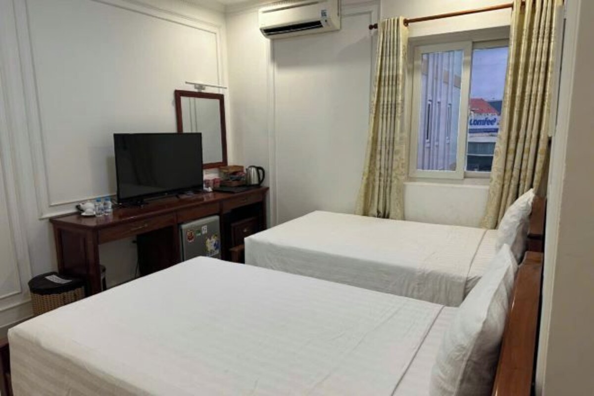 Une chambre d’hôtel avec deux lits, un bureau avec une télévision et une fenêtre avec des rideaux.