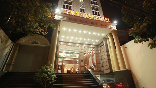 La entrada del Hotel Thanh Tai con señalización iluminada, una escalera y un interior acogedor visible a través de puertas de cristal.