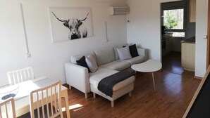 A modern living room with a sofa, a small round table, and a dining table with chairs. There is a kitchen visible through an open doorway. - Vacation home Chiara in Ilfeld, idyllic directly in the countryside!!!  (Harztor)