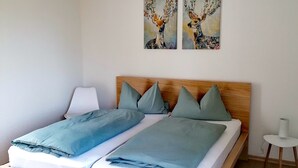 A double bed with a wooden headboard, two matching pillows, and a blue blanket. There are two wall-mounted paintings above the bed. - Vacation home Chiara in Ilfeld, idyllic directly in the countryside!!!  (Harztor)