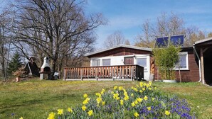 A house with a wooden deck, a chimney, and a garden with yellow and blue flowers. - Vacation home Chiara in Ilfeld, idyllic directly in the countryside!!!  (Harztor)