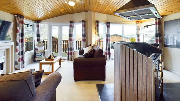 A spacious living area with a fireplace, a sofa, a coffee table, and a large window with curtains. - Lovely 3-bed House in Carnforth (Carnforth)