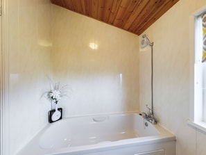 A bathroom with a white bathtub, wooden ceiling, and a shower head. - Lovely 3-bed House in Carnforth (Carnforth)