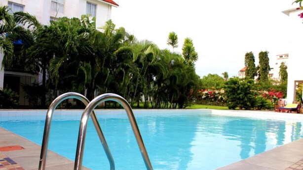 A swimming pool with metal railings, surrounded by lush greenery and a building in the background. - Stay.Plus Nyandarua Road Apartment Nyali (Mombasa)