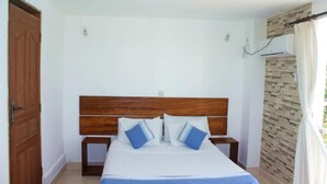 A bedroom with a wooden headboard, a bed with blue bedding, two bedside tables, and a brick-patterned wall. - Stay.Plus Nyandarua Road Apartment Nyali (Mombasa)